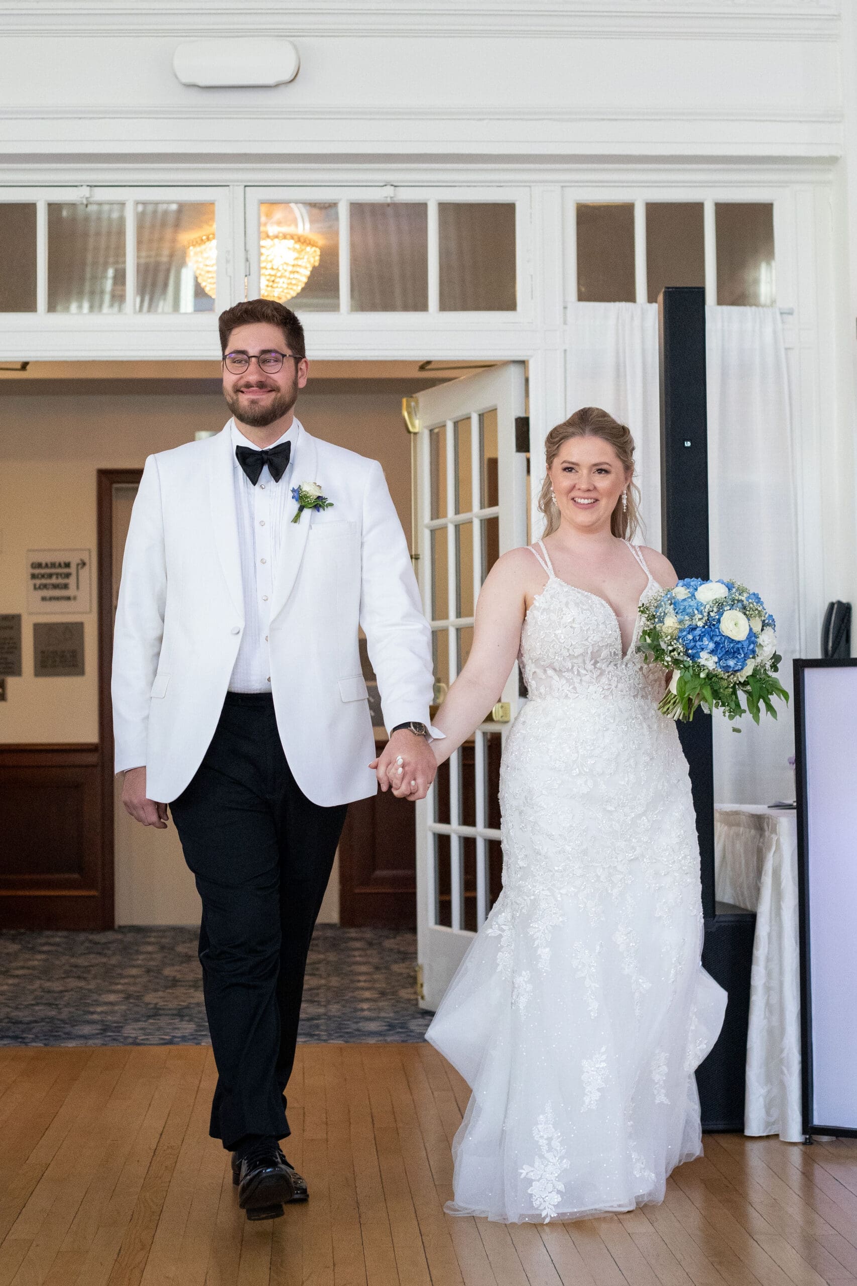 Bride and groom enter their reception featuring fit and flare dress and white tuxedo 